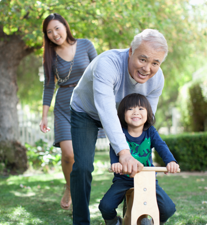 asian grandfather pushing grandchild on toy while mom looks on