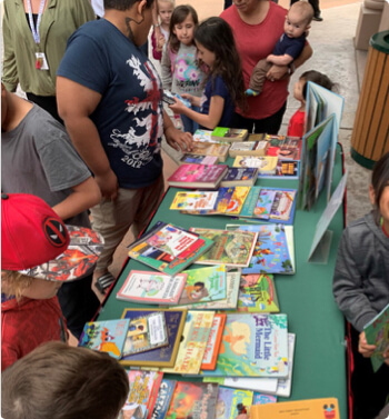 children and adults surrounding books that are spread on a table