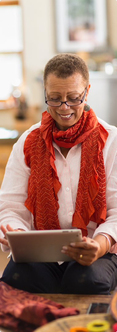senior woman with glasses and red scarf working on ipad